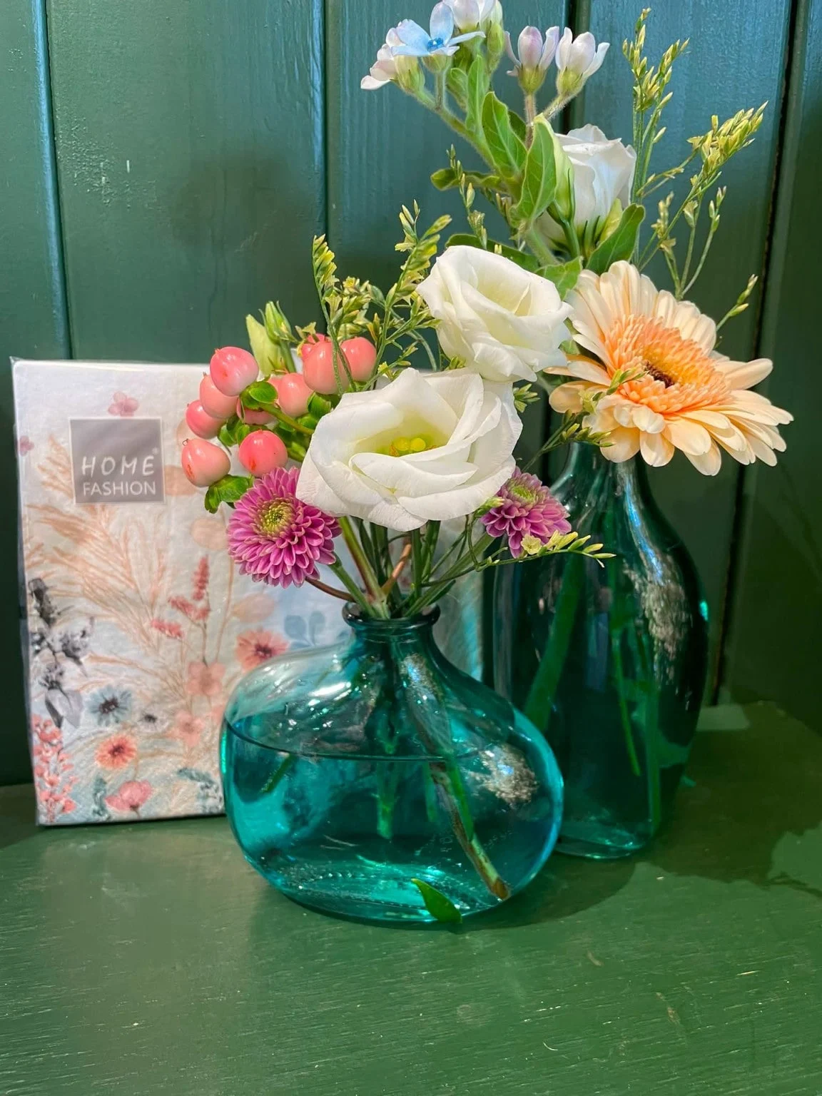 Håndbundet buket med lisianthus og gerbera i en grøn glasvase