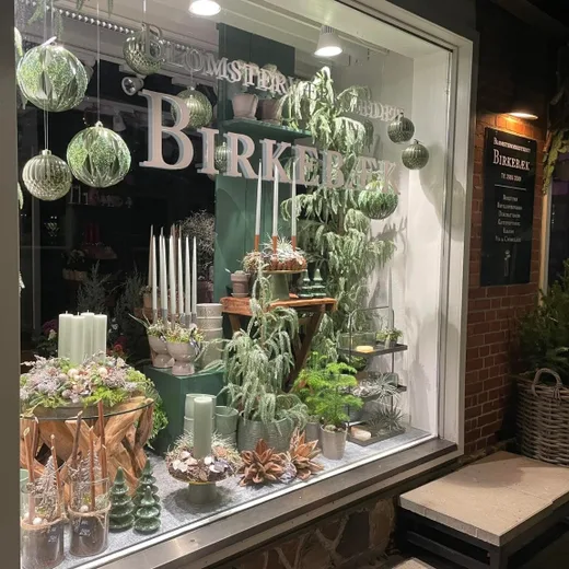 Butiksfacaden hos Blomsterværkstedet Birkebæk oplyst en vinteraften
